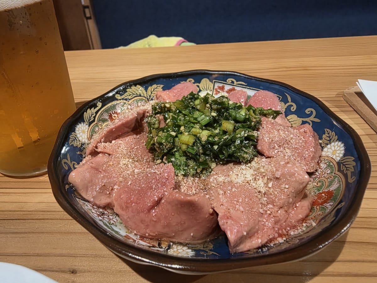 染付の小皿に円状に並べられた淡いピンク色のレバー。中央に刻んだニラのタレがのり、全体にすりおろしたニンニクがかかっている。左手前には生ビールのジョッキ