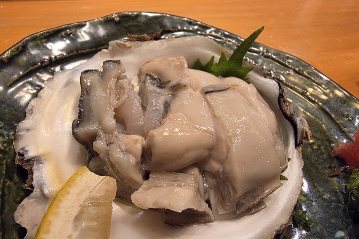 殻に盛られた岩ガキ。大ぶりの身がぶつ切りにされ、レモンと大葉が添えられている